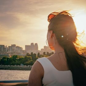 A woman looks toward a city at sunset.